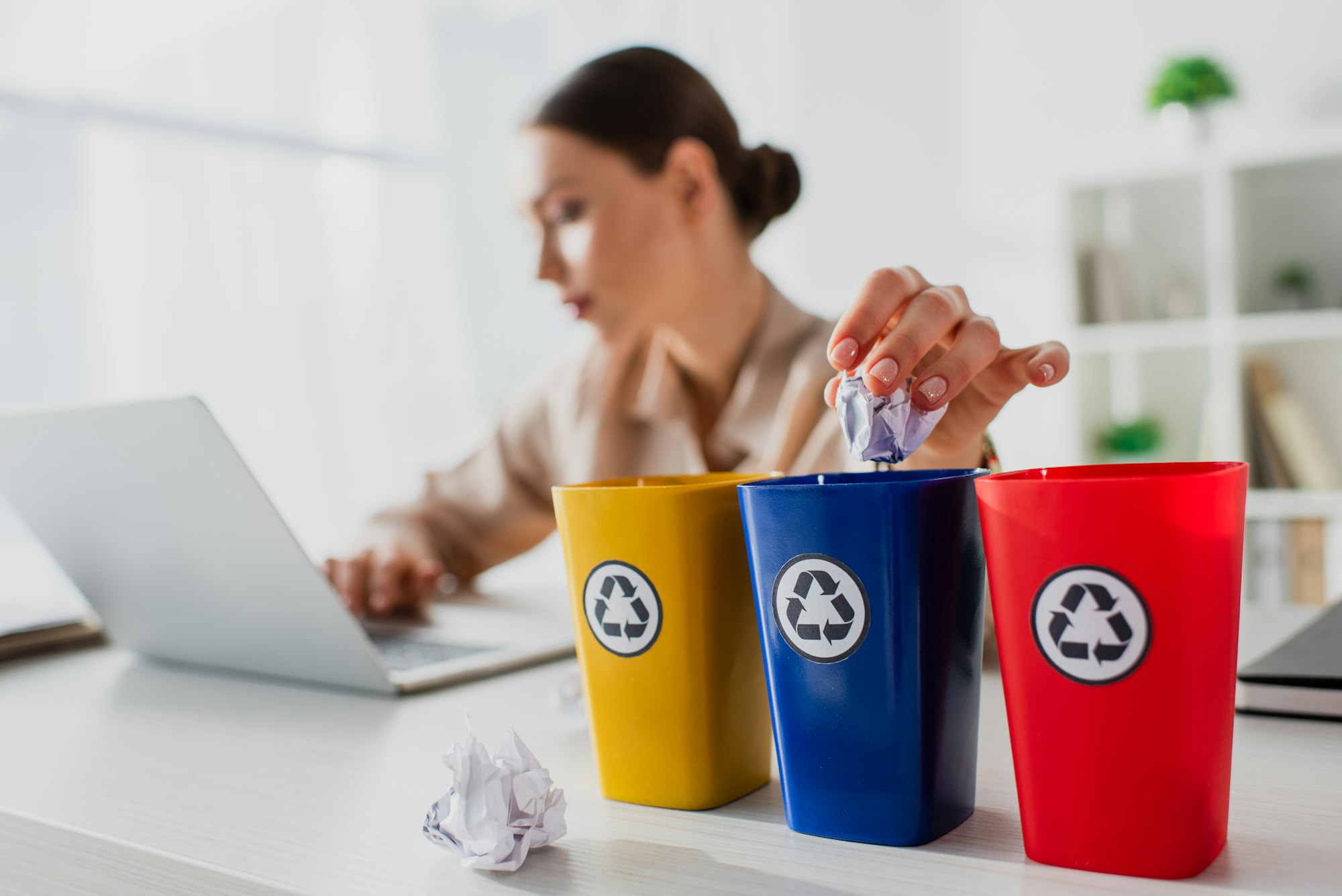 selective focus of businesswoman throwing crumpled papers into recycling buckets while working on